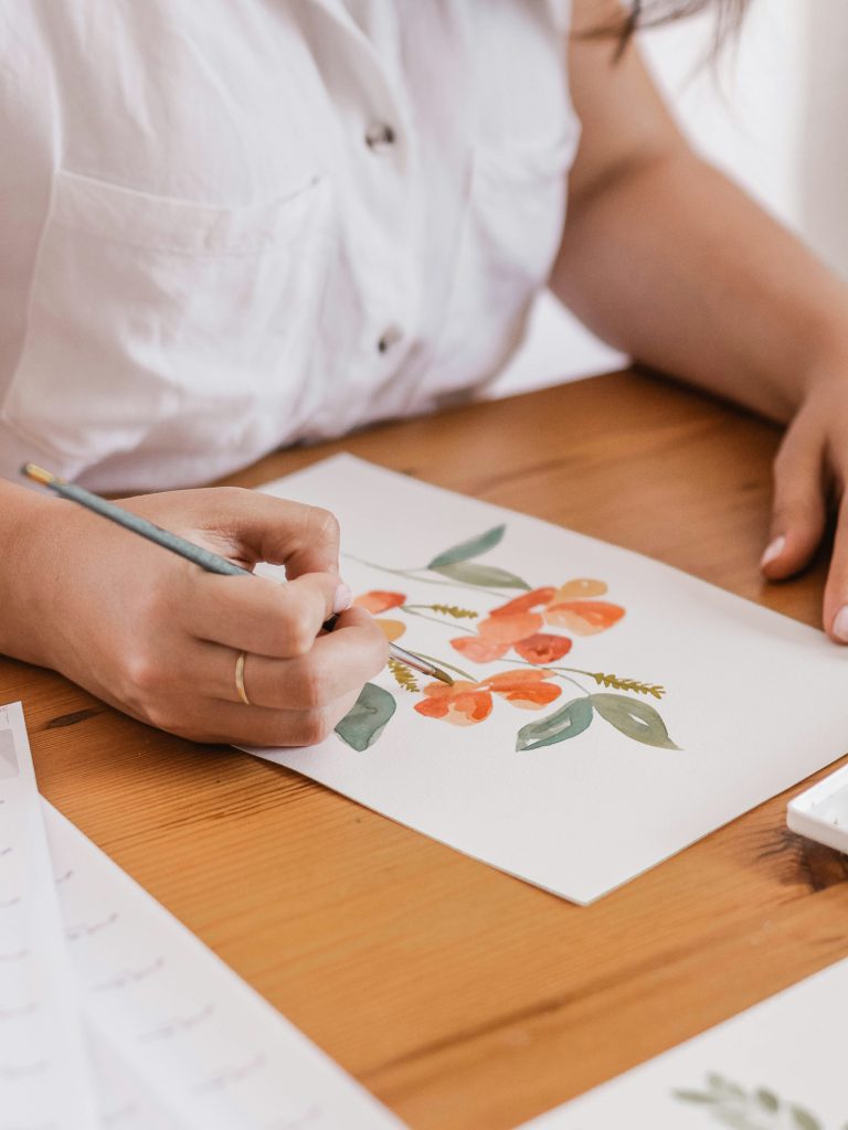 a woman's hand, painting a flower with watercolor paints